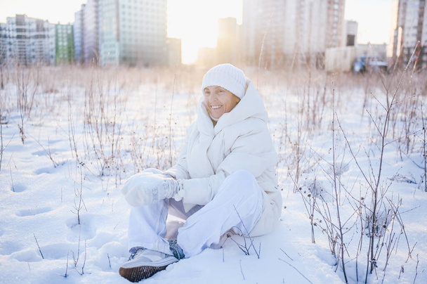 Heureuse femme mûre âgée en tenue chaude blanche jouant avec la neige en hiver ensoleillé à l'extérieur. Retraités en bonne santé vacances vacances activités d'hiver, concept de mode de vie actif - Photo, image