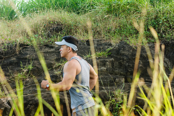 Vista lateral de um homem focado e sério correndo pelo campo. Exercício aeróbico e exercício cardio ao ar livre. - Foto, Imagem