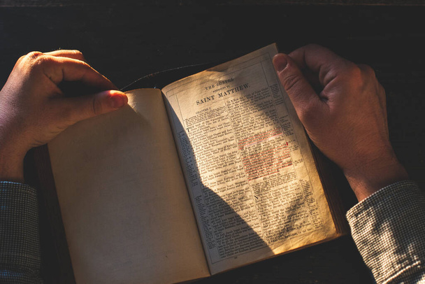 祈り、古い開いている本の上の男の手聖書、木製の机の背景. - 写真・画像
