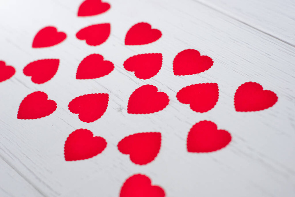 Kleine rode hartjes gemaakt van papier gelijkmatig gevoerd op een witte oude houten achtergrond.Concept van textuur, Valentijnsdag.                          - Foto, afbeelding