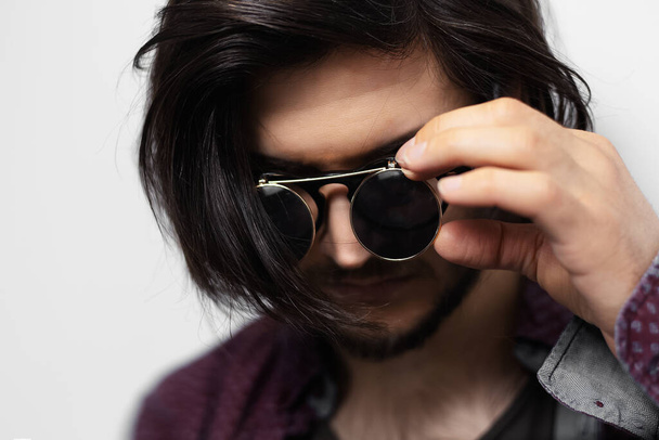Retrato de cerca de un joven con el pelo largo usando gafas de sol redondas. - Foto, Imagen
