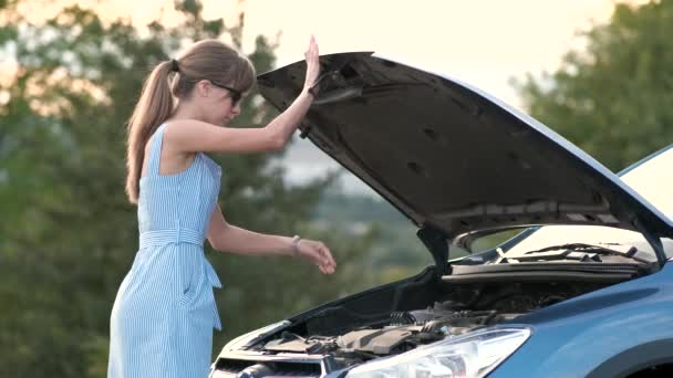 Sconcertato giovane donna conducente in piedi vicino a una macchina rotta con cappuccio aperto ispezionare il suo motore del veicolo. - Filmati, video