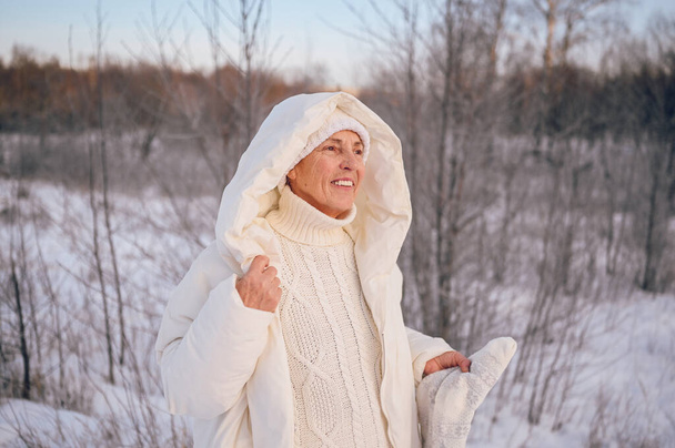 Szczęśliwy starszy starszy kobieta w białej ciepłej bieliźnie bawiąc się śniegiem w słonecznej zimie na świeżym powietrzu. Emeryci zdrowi ludzie wakacje wakacje zimowe zajęcia, koncepcja aktywnego stylu życia - Zdjęcie, obraz