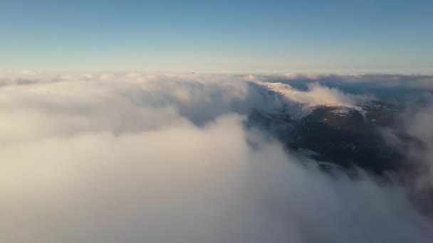 Vista aérea desde arriba de nubes blancas hinchadas que cubren las cumbres nevadas de las montañas en un día soleado brillante. - Imágenes, Vídeo