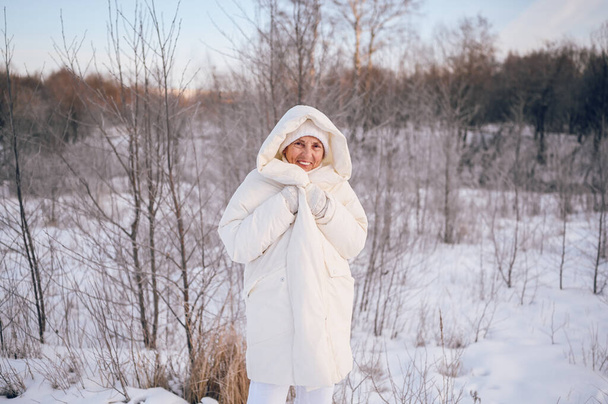 晴れた冬の屋外で雪と遊ぶ白い暖かい外耳部で幸せな高齢者の高齢者の成熟した女性。退職健康的な人々の休暇の冬の活動、アクティブなライフスタイルの概念 - 写真・画像