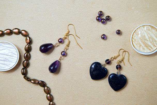 Gemstone earrings, top view. Amethysts, aventurine and glass beads on a cardboard background. Women's jewelry close-up - Foto, immagini
