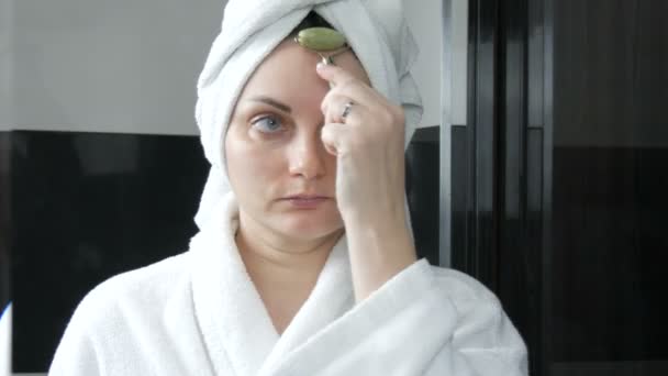 Belle femme avec serviette sur la tête faisant un massage avec un rouleau de jade pour le front du visage de pierre naturelle dans la salle de bain. Outils de beauté chinois. Massage lymphatique de la peau contre les rides vieillissantes - Séquence, vidéo