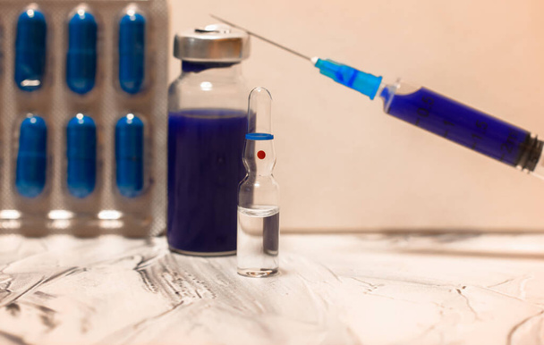 Скляна медична прозора ампула на столі, пов'язка, шприц і сині таблетки. Вакцина проти грипу ізольована, пандемія коронавірусу та медична допомога. Високоякісна фотографія
 - Фото, зображення