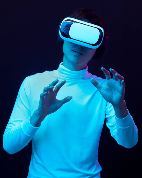 Νεαρός Ασιάτης φοράει γυαλιά εικονικής πραγματικότητας βλέποντας βίντεο 360 μοιρών σε νέον φως, Τεχνολογία έννοια. - Φωτογραφία, εικόνα
