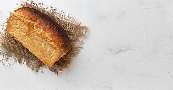 Буханка белого деревенского хлеба на льняной подкладке на белом столе. Идея для малого бизнеса, изготовленный на заказ хлеб из теста. Вид сверху с пространством для копирования - Фото, изображение