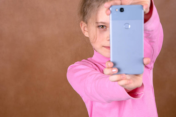 Retrato de una niña alegre tomando una selfie sobre fondo marrón borroso con espacio para copiar - Foto, imagen
