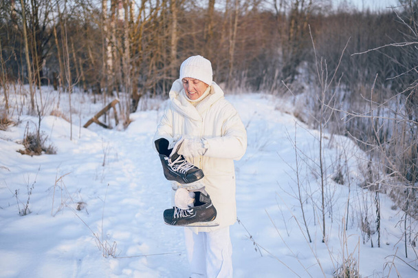 Happy elderly senior mature woman in white warm outwear playing with ice skates in sunny snowy winter outdoors. Retired healthy people holiday vacation winter activities, active lifestyle concept - Photo, Image