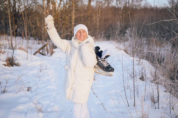 Щаслива літня старша зріла жінка в білому теплому одязі грає з льодовими ковзанами в сонячну засніжену зиму на відкритому повітрі. Відпустка здорових людей відпочинок зимові заходи, концепція активного способу життя
 - Фото, зображення