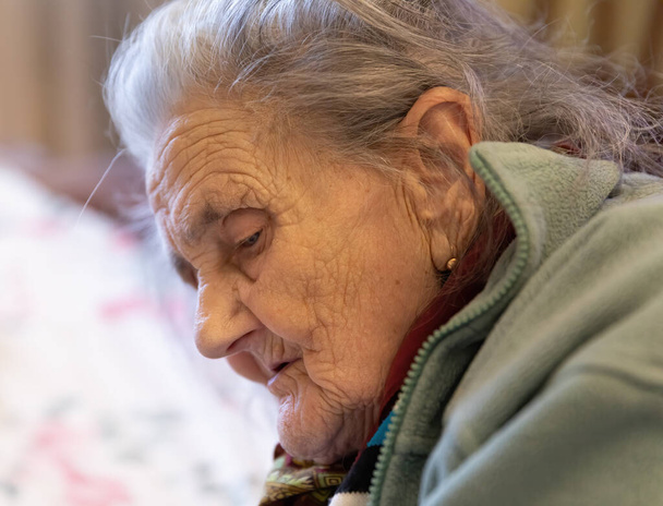 Öregasszony. Egy nagyon öreg, depressziós nő portréja, aki otthon ül az ágyon. - Fotó, kép