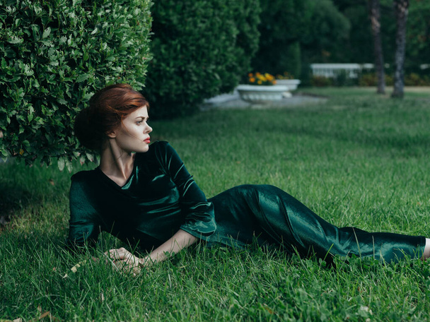 Beautiful woman in a green dress outdoors lies on the grass gothic style masquerade charm - Fotoğraf, Görsel