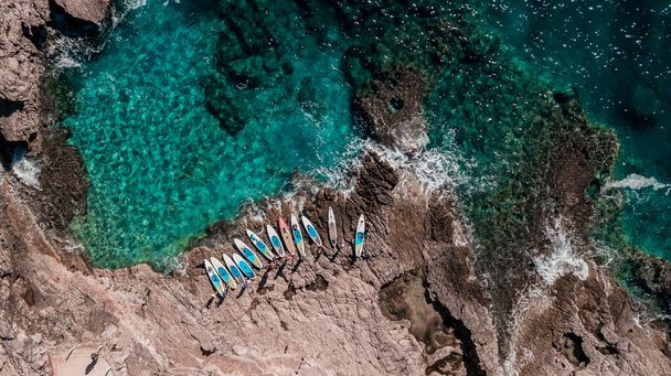 Hermosa playa rocosa con SUP stand up paddle boards y con agua turquesa en Montenegro. Vista desde arriba con dron - Foto, imagen