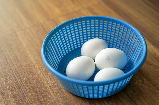 4 huevos de pollo blanco en canasta de plástico azul en el suelo de madera. 1 of 4 El pollo está listo para romper la cáscara de huevo desde el interior. - Foto, imagen