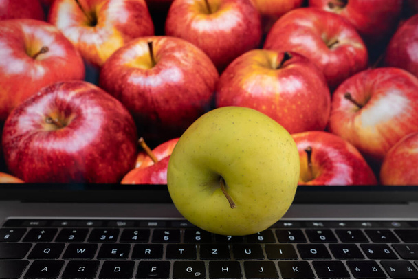 Pomme jaune sur le clavier devant un écran d'ordinateur portable plein de pommes rouges mûres juteuses - Photo, image