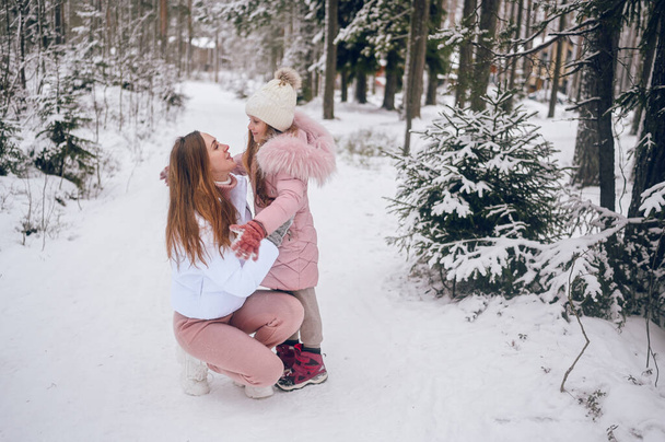 Szczęśliwa matka i dziewczynka w różowej ciepłej bieliźnie spacerując zabawy i przytulając się w śniegu biały zimowy las iglasty zima z lasów świerkowych na zewnątrz. Rodzinne zajęcia sportowe - Zdjęcie, obraz