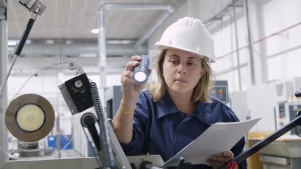 Ingénieur femelle focalisée inspectant la machine avec la lampe de poche - Séquence, vidéo