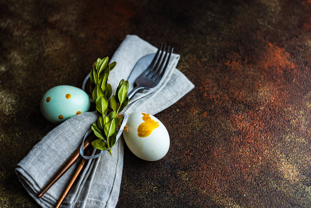 Pasen bestek instelling met gekleurde eieren en boxwood bladeren op betonnen achtergrond met kopieerruimte - Foto, afbeelding