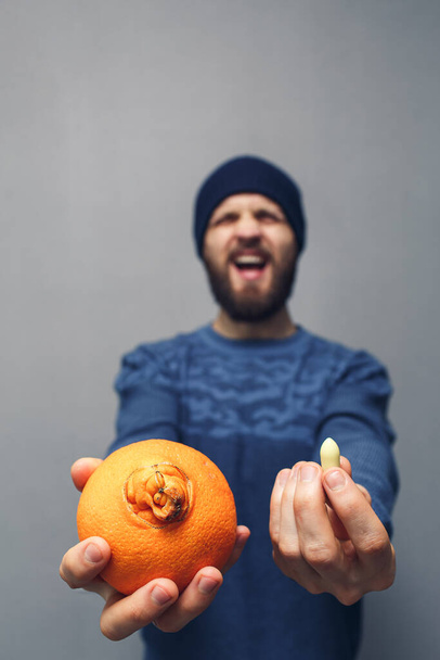 Een man schreeuwt in problemen door aambeien. Een man met een baard heeft een sinaasappel en een zetpil voor aambeien in zijn handen. Hemorroïden concept - Foto, afbeelding