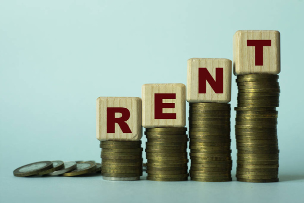 RENT - word on wooden cubes. Which stand on stacks of coins on a light background. Business concept - Фото, изображение