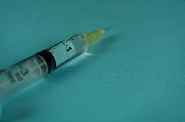 A syringe with liquid drop on turquoise background - Φωτογραφία, εικόνα