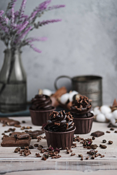 Several muffins or cupcakes with chocolate shaped cream at white table. Festive candle burns on a chocolate cake. - 写真・画像