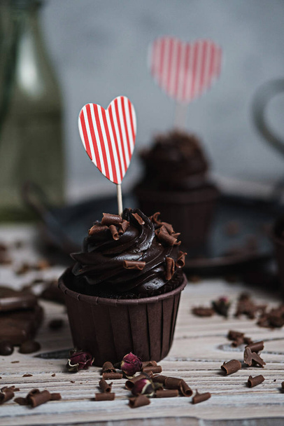 Several muffins or cupcakes with chocolate shaped cream at white table. A holiday card in the form of a heart for St. Valentines Day in one of them. - Fotó, kép