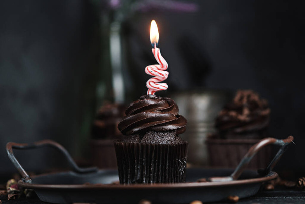 Several muffins or cupcakes with chocolate shaped cream at black table. Festive candle burns on a chocolate cake - Foto, immagini