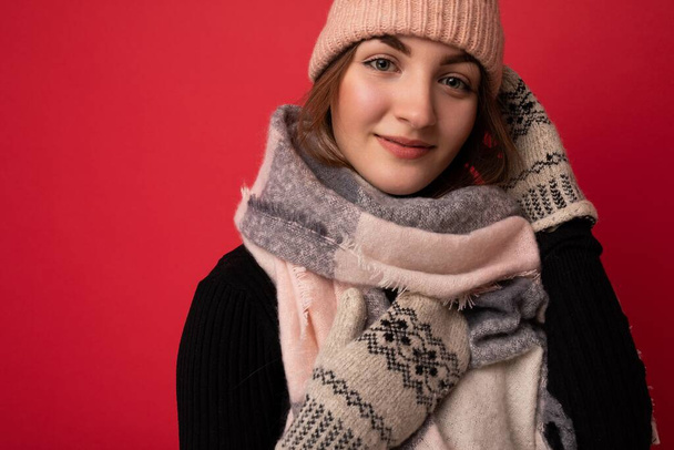 Closeup photo of beautiful happy cute young brunette woman isolated over red background wall wearing winter scarf mittens and warm hat looking at camera - Foto, imagen