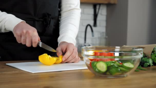 Chef-kok in zwarte schort gesneden verse gele peper aan boord in huis keuken - Video