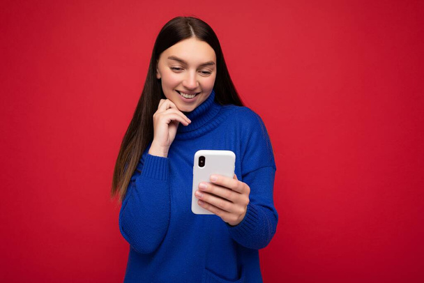 Fotoshooting von attraktiven positiv gut aussehende junge Frau trägt lässig stilvolles Outfit posiert isoliert auf dem Hintergrund mit leeren Raum halten in der Hand und mit Handy-Nachrichten-SMS Blick auf - Foto, Bild