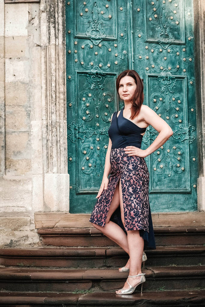 Mooie vrouw in een sexy jurk staat op de trap op de achtergrond van een oud huis. Kopieer, lege ruimte voor tekst. - Foto, afbeelding