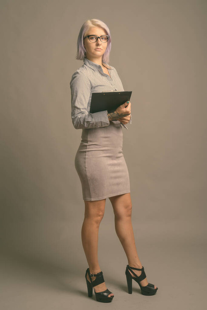 Jeune belle femme d'affaires avec des cheveux courts et colorés sur fond gris - Photo, image