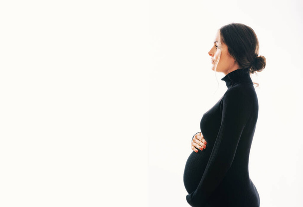 Stúdió anyaság portré gyönyörű fiatal nő, pózol a fehér háttér, visel fekete teknős nyak ruha  - Fotó, kép