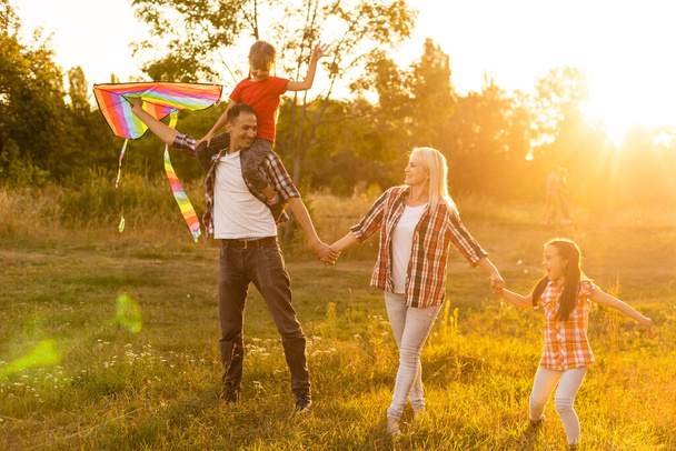 Felice padre di famiglia di madre e figlie lanciare un aquilone sulla natura al tramonto - Foto, immagini