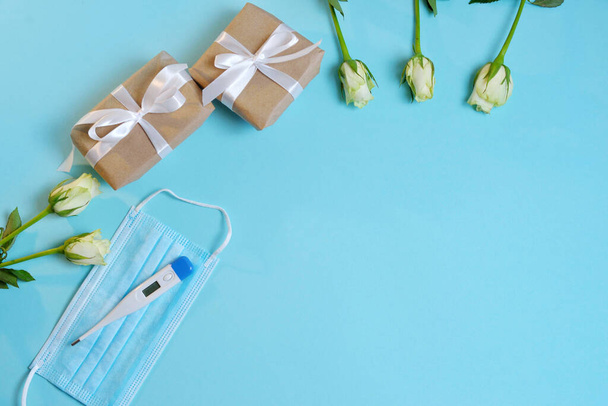 белые розы, медицинская маска, термометр, подарки на бумаге, завязанные белой атласной лентой на синем фоне. Концепция Дня доктора, плоский вид сверху - Фото, изображение