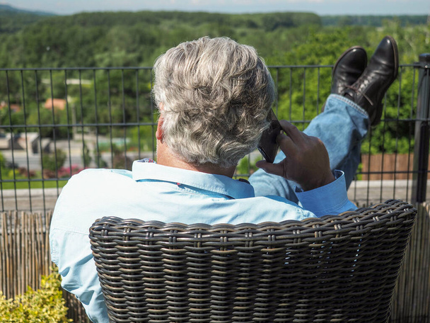 Uomo d'affari anziano con smartphone che fa telefonate in giardino. Colpo orizzontale. - Foto, immagini
