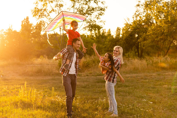 Ευτυχισμένη οικογένεια με χαρταετό να παίζει το ηλιοβασίλεμα στο γήπεδο - Φωτογραφία, εικόνα