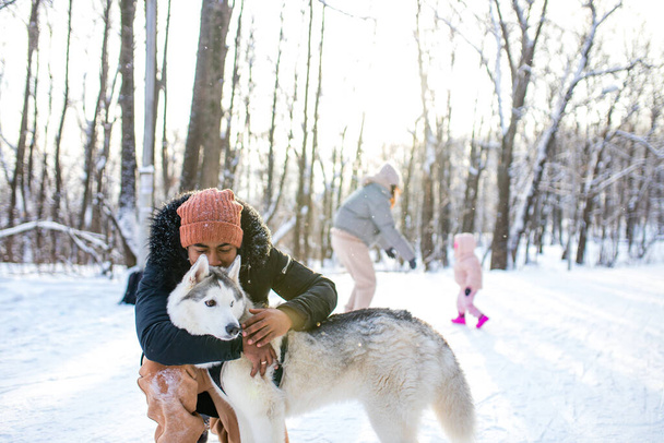 mixed race man hug his dog husky in winter forest park - Fotó, kép