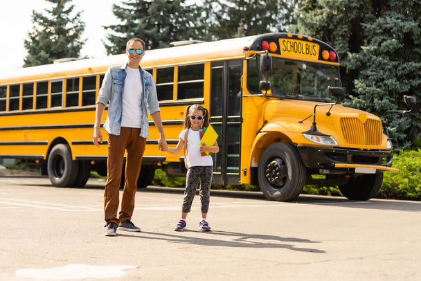 Dívka s otcem se vrací do školy poblíž školního autobusu - Fotografie, Obrázek