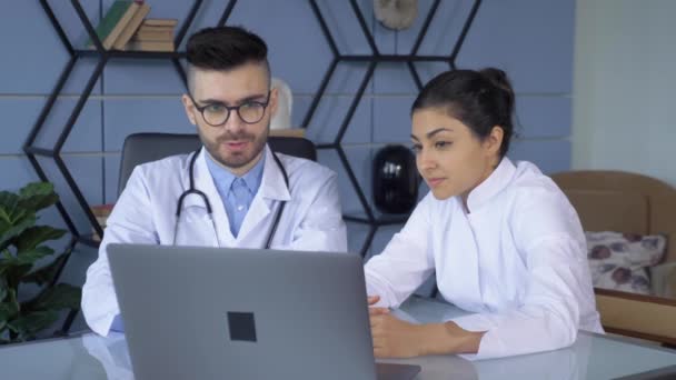 Два лікарі, чоловік і жінка, які працюють на комп "ютері або в лаптопі, знаходяться в яскравому офісі лікарні - Кадри, відео