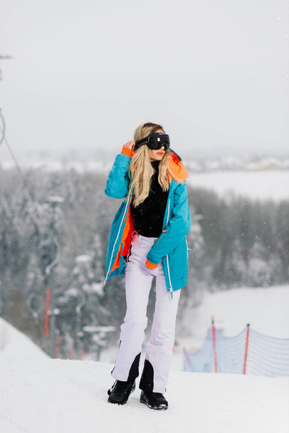 Žena ve sportovním oblečení snowboardista pózuje ve slunečních brýlích se snowboardem - Fotografie, Obrázek