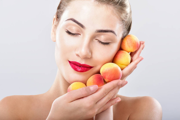 Beautiful woman holding a juicy apricots, peaches. Perfect skin. Fruit facial masks. Professional makeup. - Foto, afbeelding