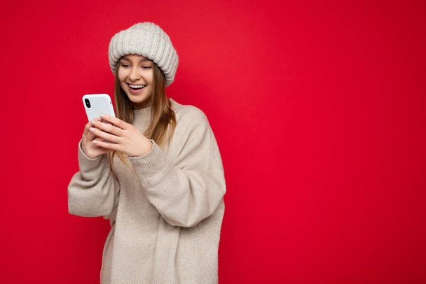 Красивая молодая женщина в повседневной одежде, стоящая изолированно над фоном серфинга в Интернете по телефону, глядя на мобильный экран - Фото, изображение