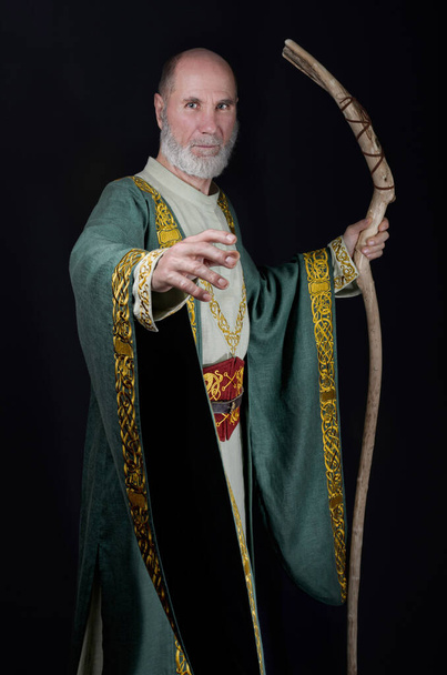 金の刺繍が施された濃い緑色のローブを着た古いウィザード。魔法の杖を手に. - 写真・画像