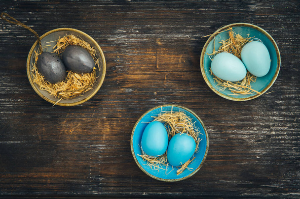 Drei kleine bunte Schalen gefüllt mit Ostereiern in derselben Farbe auf rustikalem Holz, Osterdekoration, schäbiger Stil, Draufsicht mit Kopierraum - Foto, Bild