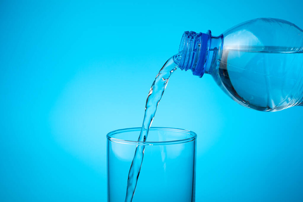 Gießen Sie in einem leeren Glas frisches Wasser auf einen blauen Hintergrund. - Foto, Bild